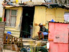 A man sits outside a makeshift home in a slum in Cape Town, South Africa